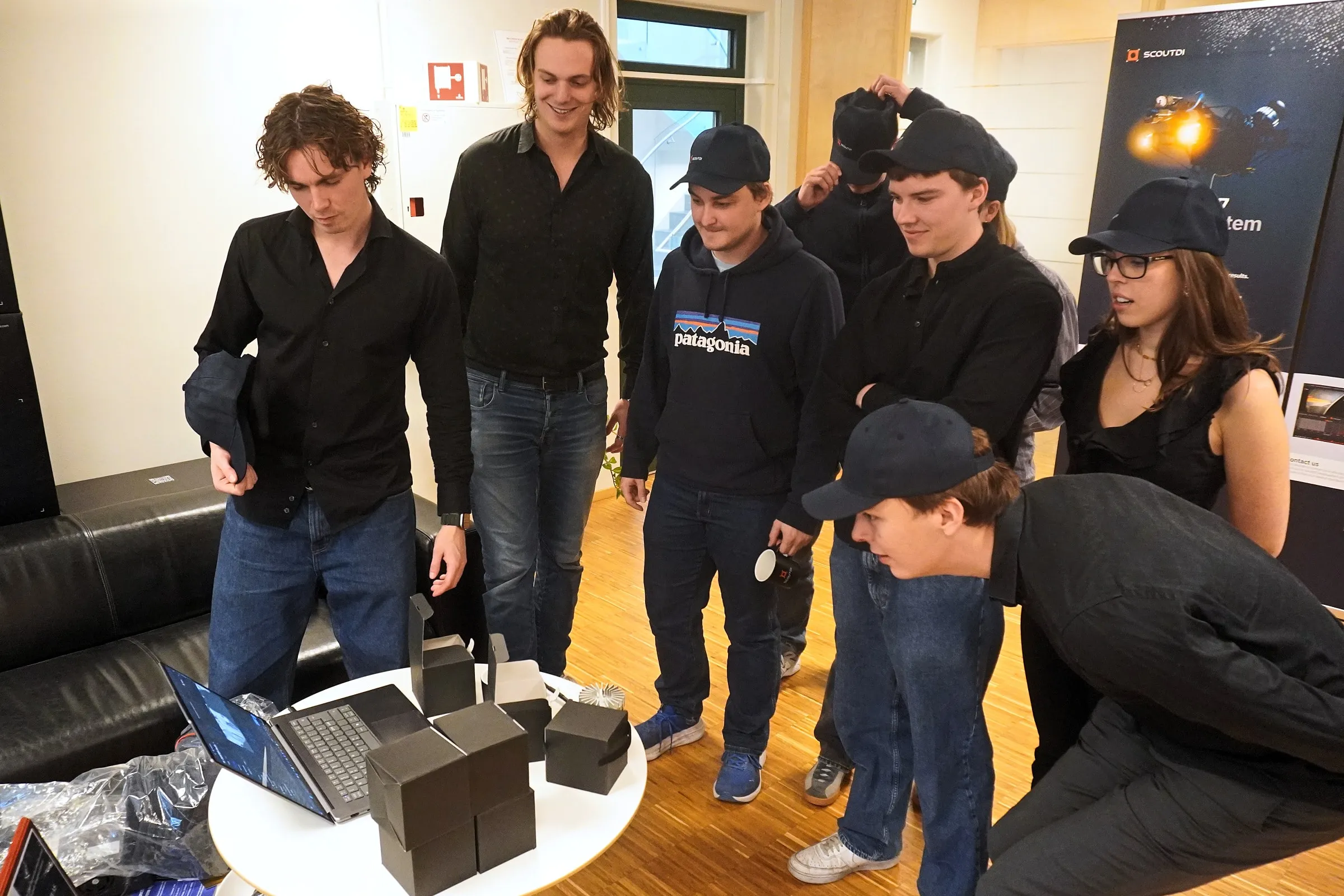 Mobula team members gathered around a laptop and a table of black boxes at ScoutDI's office
